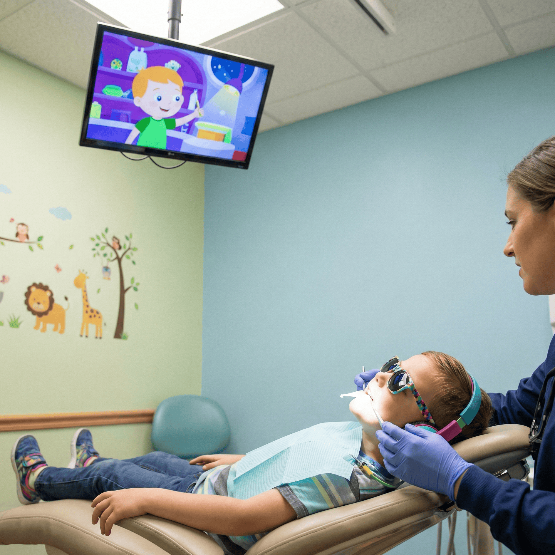 Child calmly resting in a dental chair while watching a cartoon as a pediatric dentist uses gentle distraction techniques to manage dental anxiety and promote a relaxed experience.
